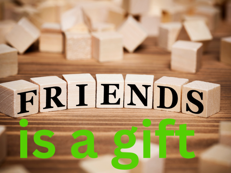 The image shows a close-up of small wooden blocks spelling the word "FRIENDS" in capital letters. These blocks are set on a wooden surface with more blocks scattered in the background. Below the blocks, the words "is a gift" are prominently written in bold green text, completing the phrase "Friendship is a gift." The overall message emphasizes the value of friendship as something precious and meaningful.